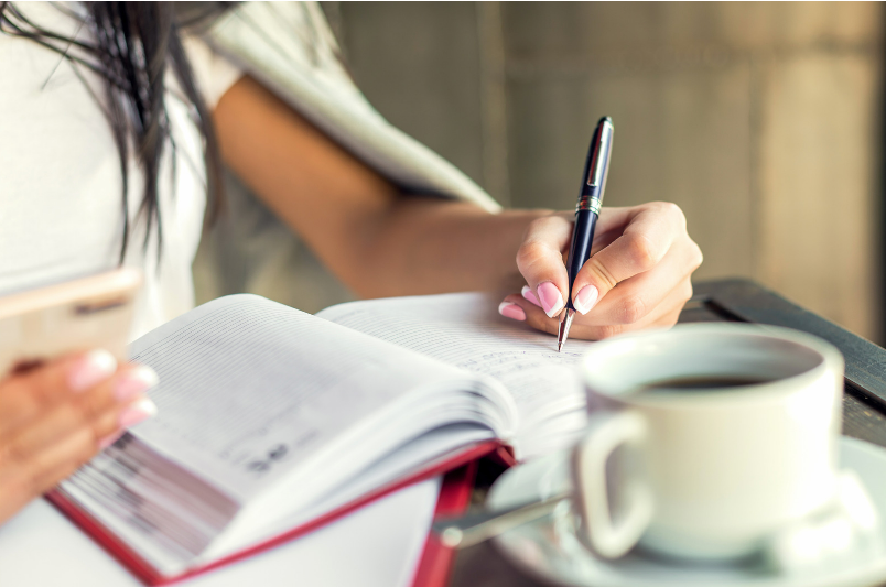 Persoon die een dagboek bijhoudt met een kopje koffie op tafel als voorbeeld van gewoontevorming.
