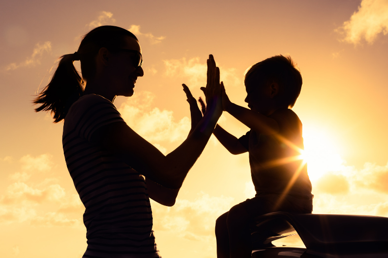 Moeder met haar kind, high five, met de ondergaande zon op de achtergrond.