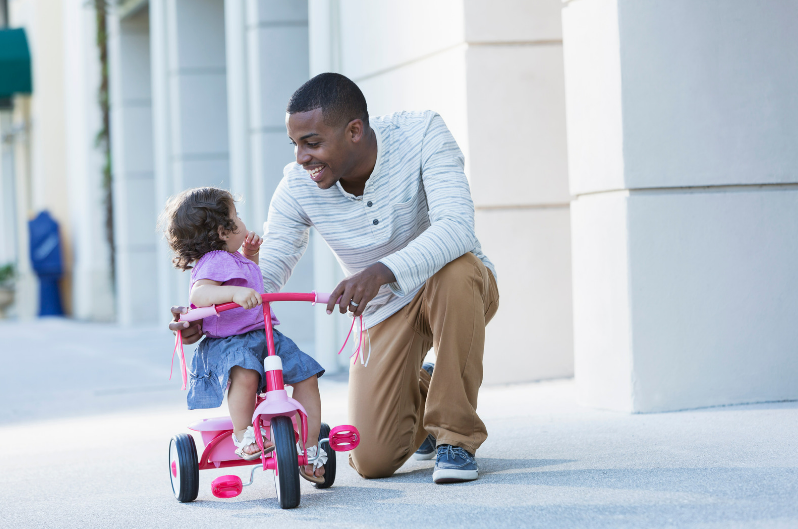 Een vader met dochter die op een driewieler rijdt.